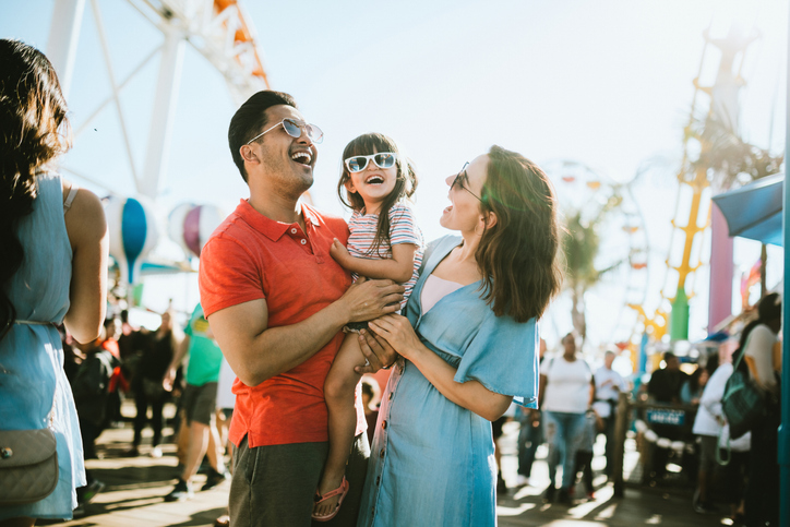 A family of three laughing and enjoying their day at an amusement park.