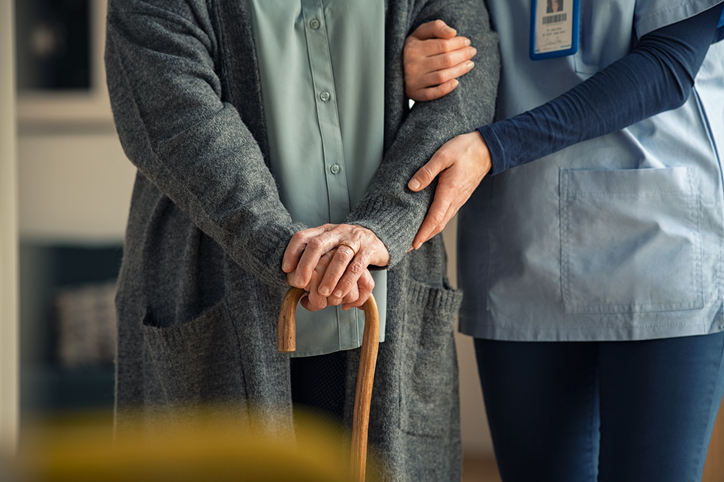 A care specialist providing support by the arm for a senior with a walking cane