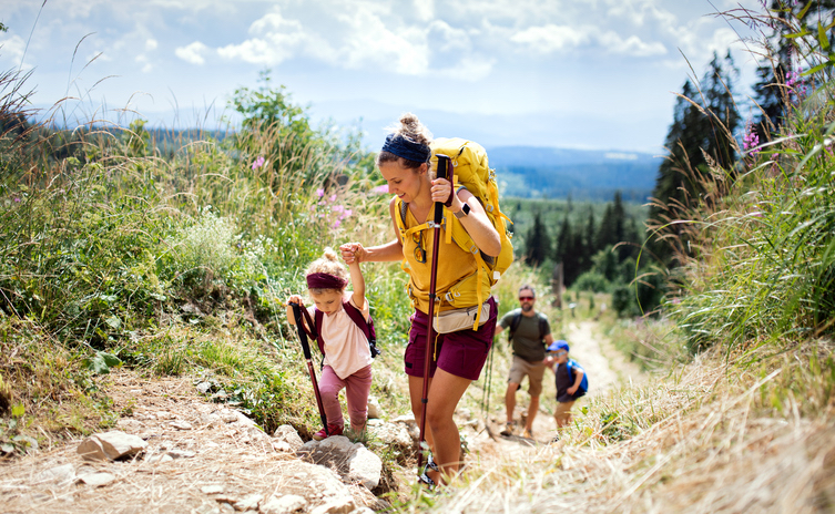 A woman and a small child are hiking up a trail. The woman is holding the child's hand.