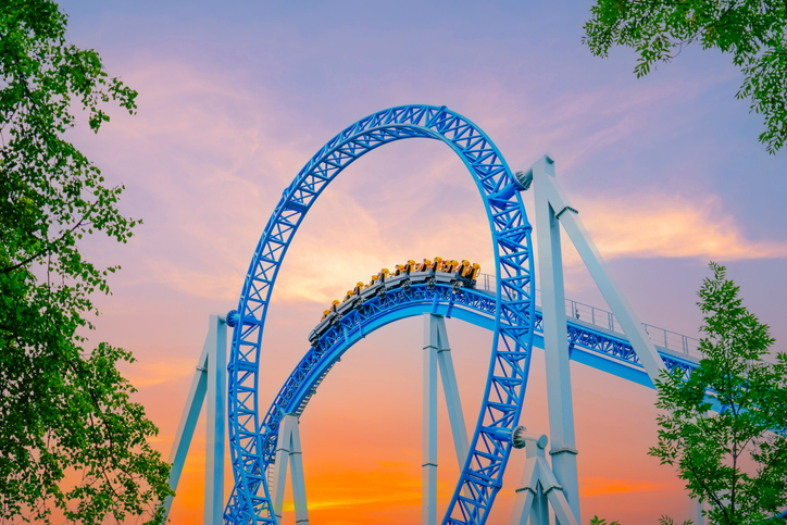 A sleek, blue and white roller coaster with a train full of riders passing a loop with a stunning sunset sky in the background.