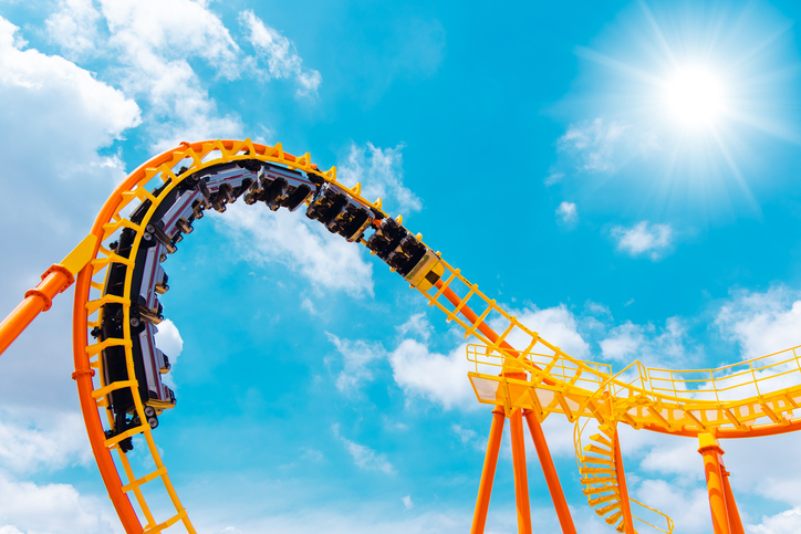 A bright orange and yellow roller coaster track with a train of cars rounding a sharp curve against a vivid blue sky.