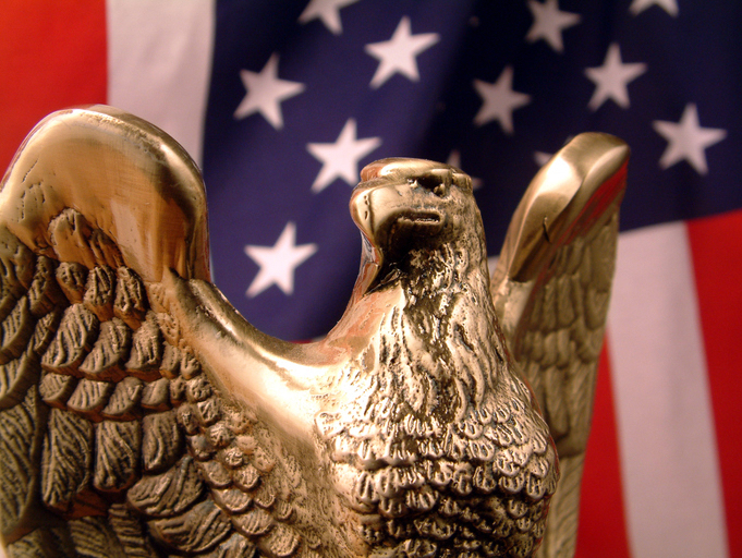 A brass eagle figurine is displayed in the foreground, with the American flag in the background.