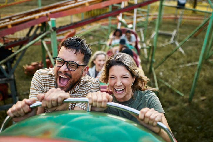 A man and a woman in the foreground scream and laugh with excitement while riding a roller coaster.