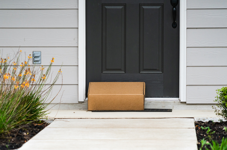  A cardboard package sits on a front porch in front of a dark-colored door.