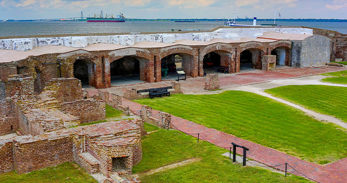 Aerial view of Fort Sumter's courtyard with brick walls, arches, grass, and the Charleston skyline.