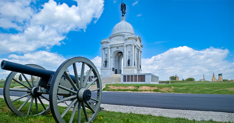 Civil War cannon and the Pennsylvania Memorial at Gettysburg National Military Park under a blue sky.
