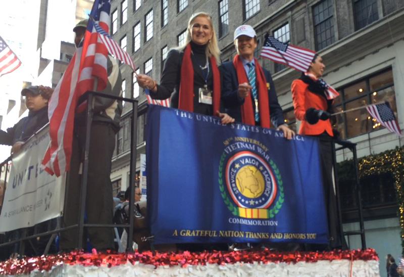 Founders Scott and Lin Higgins on the 2014 New York City Veterans Day Parade Float with the Vietnam War 50th Anniversary Commemoration Flag hanging below