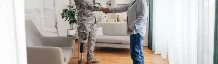 Veteran with a prosthetic leg and counselor shake hands in room