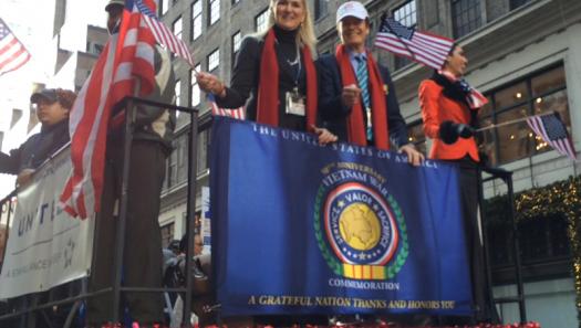 Founders Scott and Lin Higgins on the 2014 New York City Veterans Day Parade Float with the Vietnam War 50th Anniversary Commemoration Flag hanging below